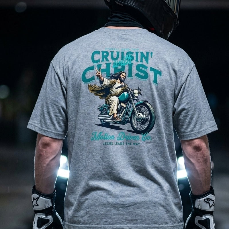 A person shown from behind wearing a heather gray t-shirt with a large graphic print on the back. The graphic features a motorcycle and an illustration of Jesus riding it, with the text 'CRUISIN' CHRIST' and 'Motion Driven Co.
