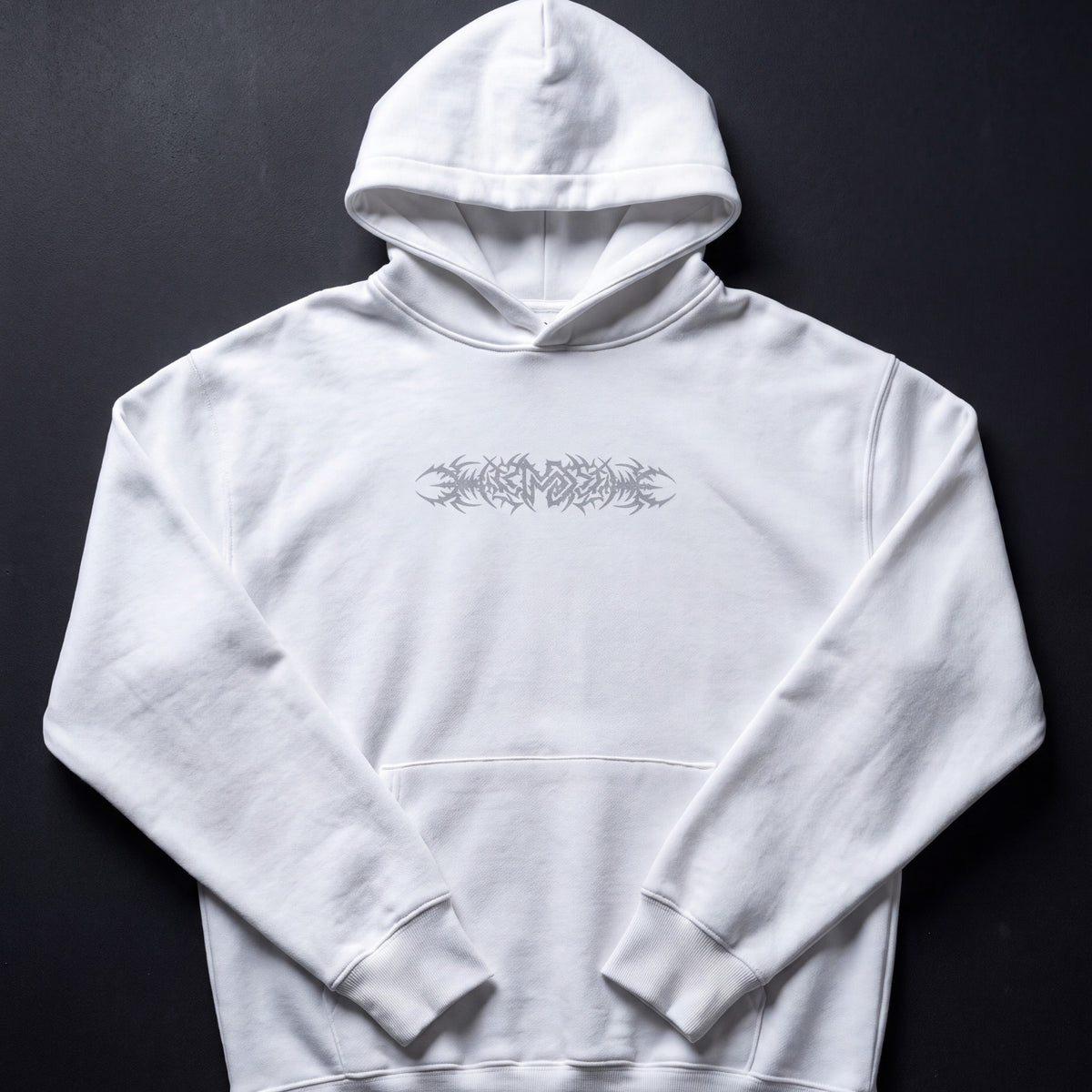 A white pullover hoodie with a gray graphic print across the chest, laid flat against a dark textured background.